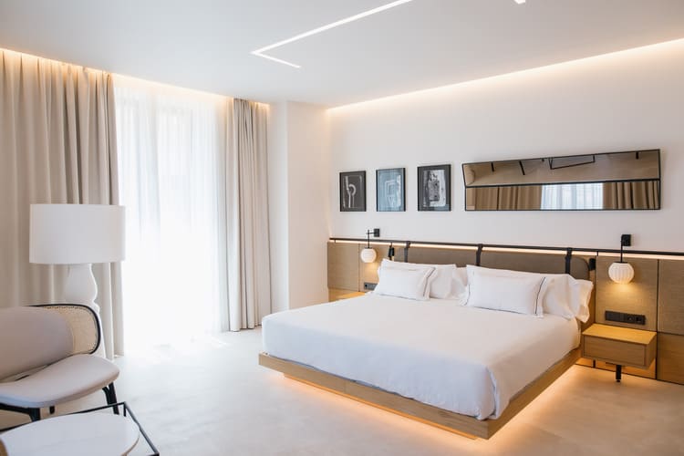 Habitación de The Bank Hotel con cama king, cabecero iluminado y ventanales.