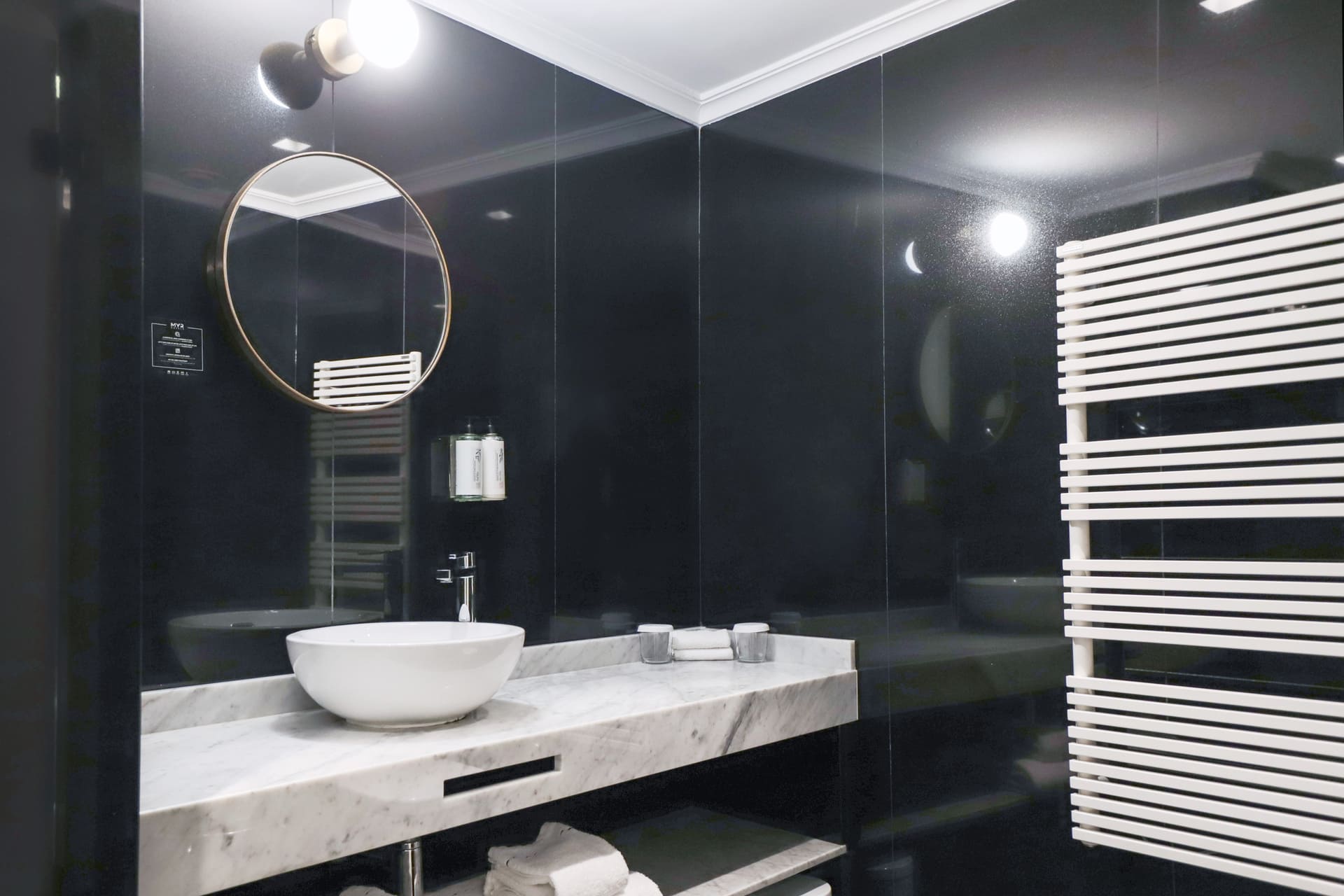 Lavabo blanco de cuenco sobre encimera en baño moderno con espejo circular y toallero radiador blanco