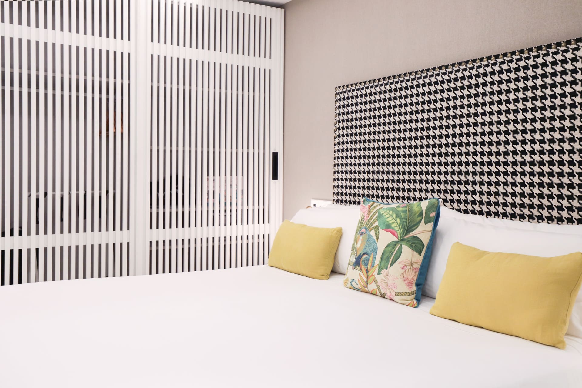 Cama de hotel con cabecera de patrón negro y blanco y cojines amarillos y tropicales