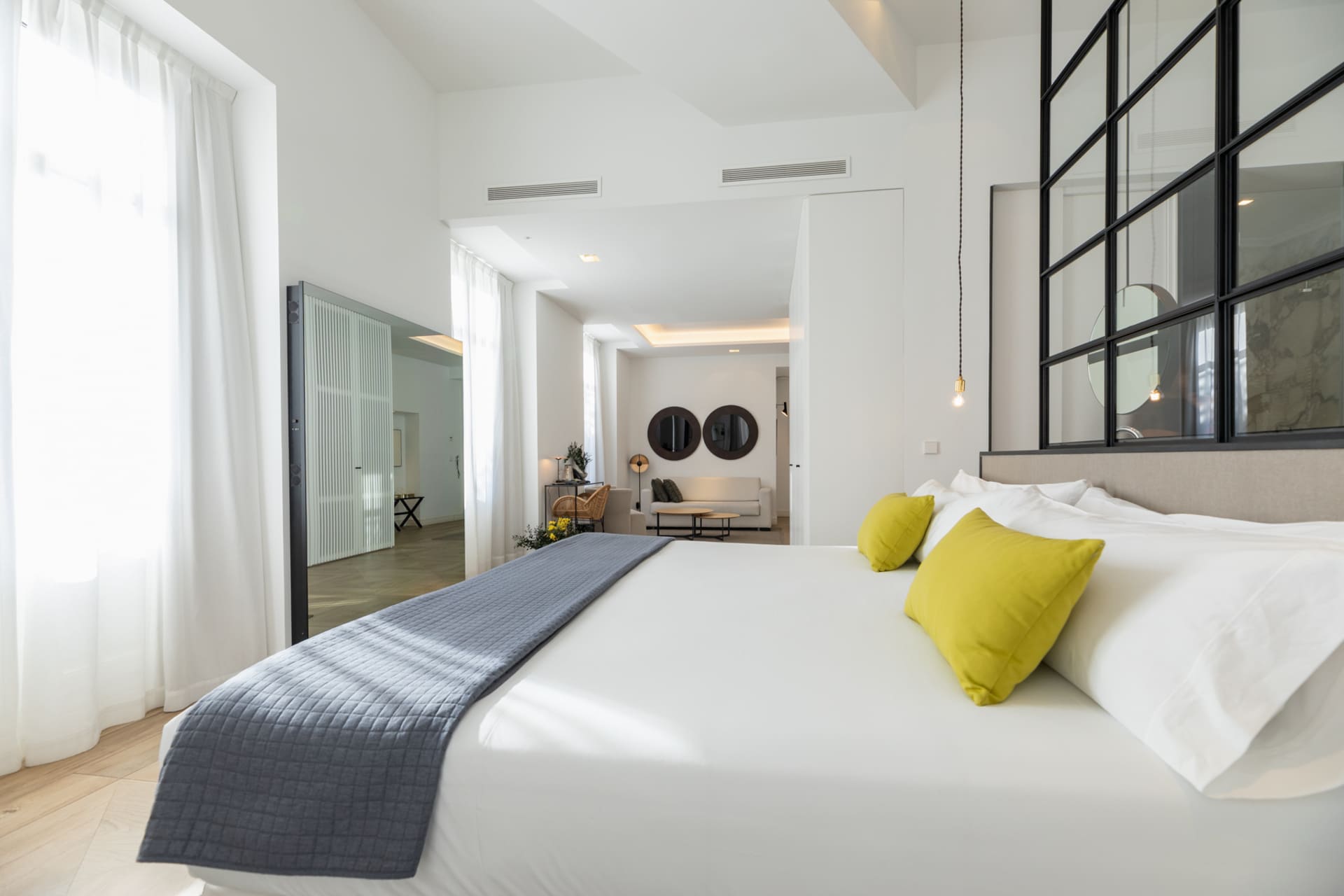 Dormitorio de suite con cama grande, cojines amarillos y separador de vidrio negro