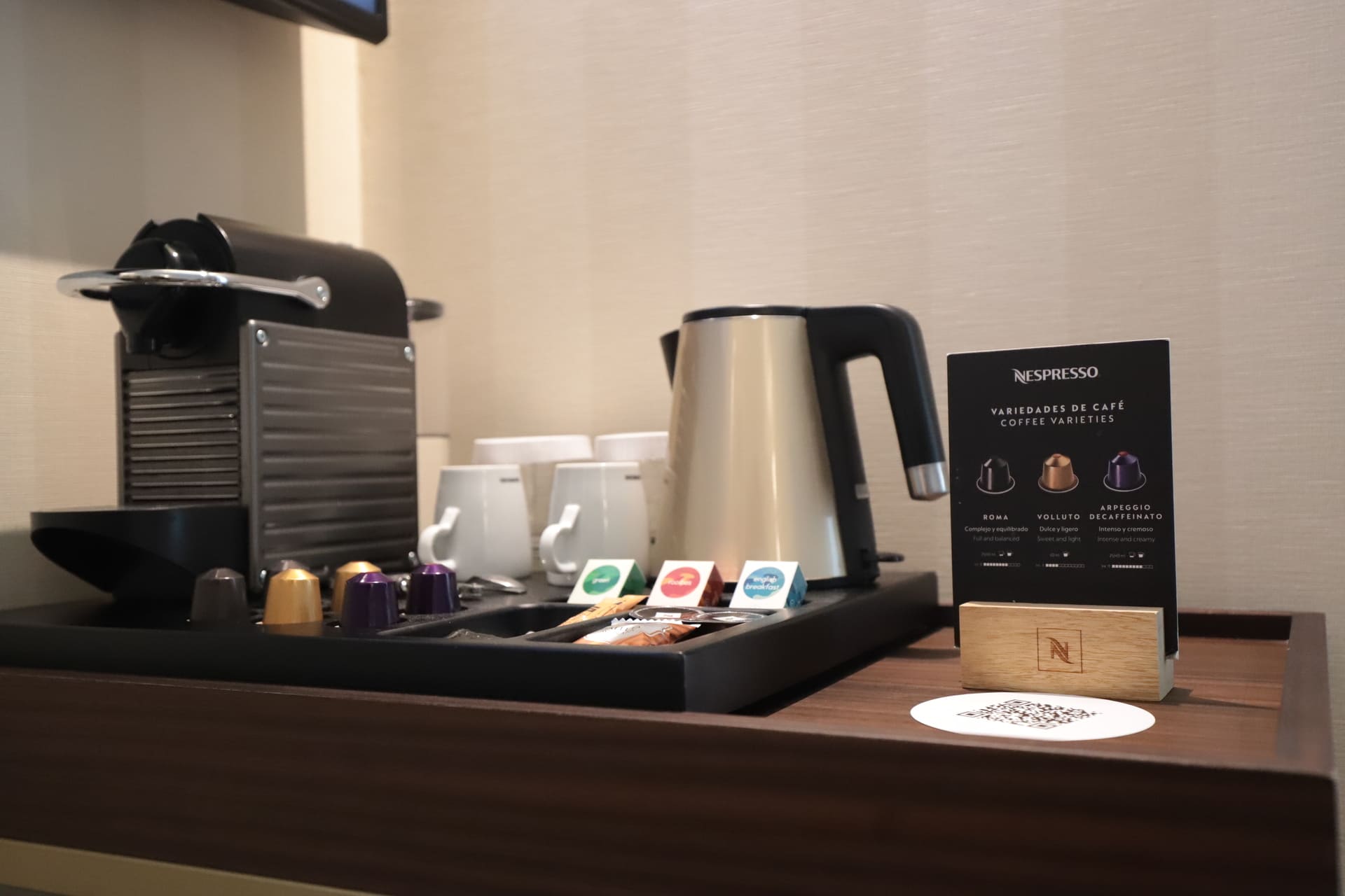 Estación de café en habitación con máquina Nespresso, hervidor y cápsulas.