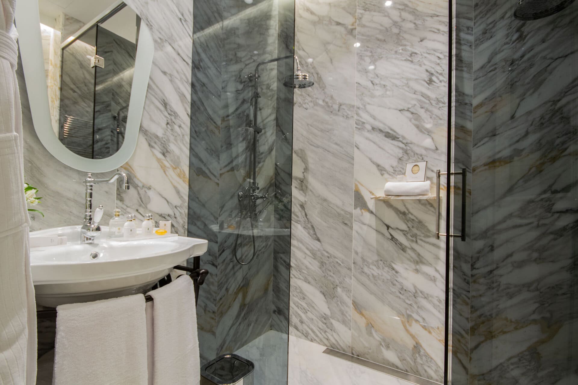 Baño de hotel con lavabo, espejo oval y ducha de vidrio