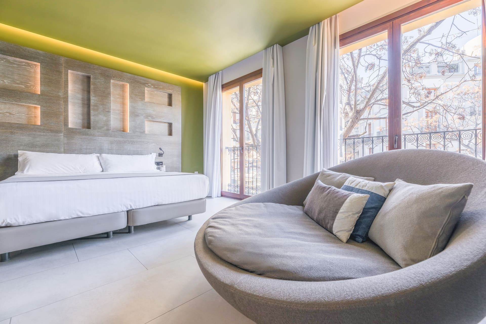 Habitación de hotel moderna con cama king y sofá curvo junto a ventanales