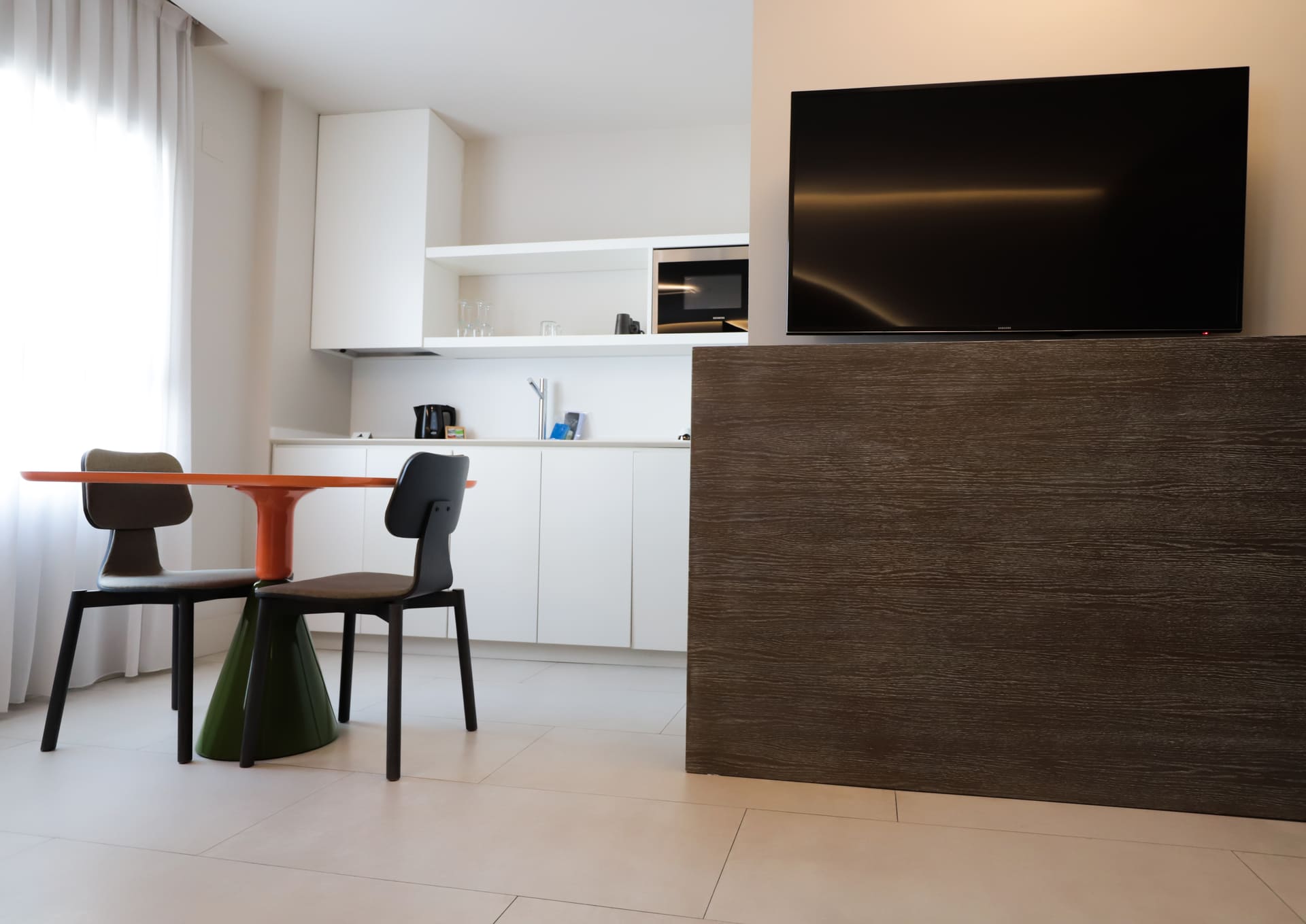 Zona de cocina abierta y comedor en habitación de hotel con mesa naranja