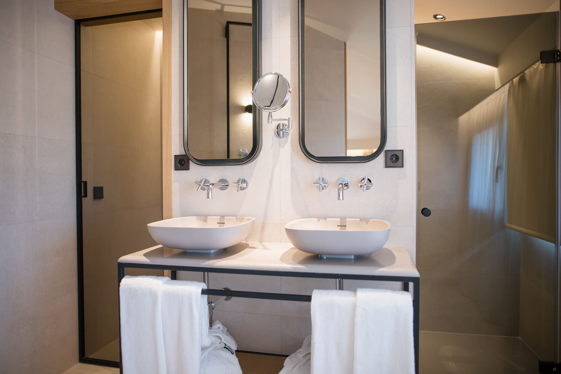 Lavabos dobles en baño de hotel con espejos ovalados y toallas blancas