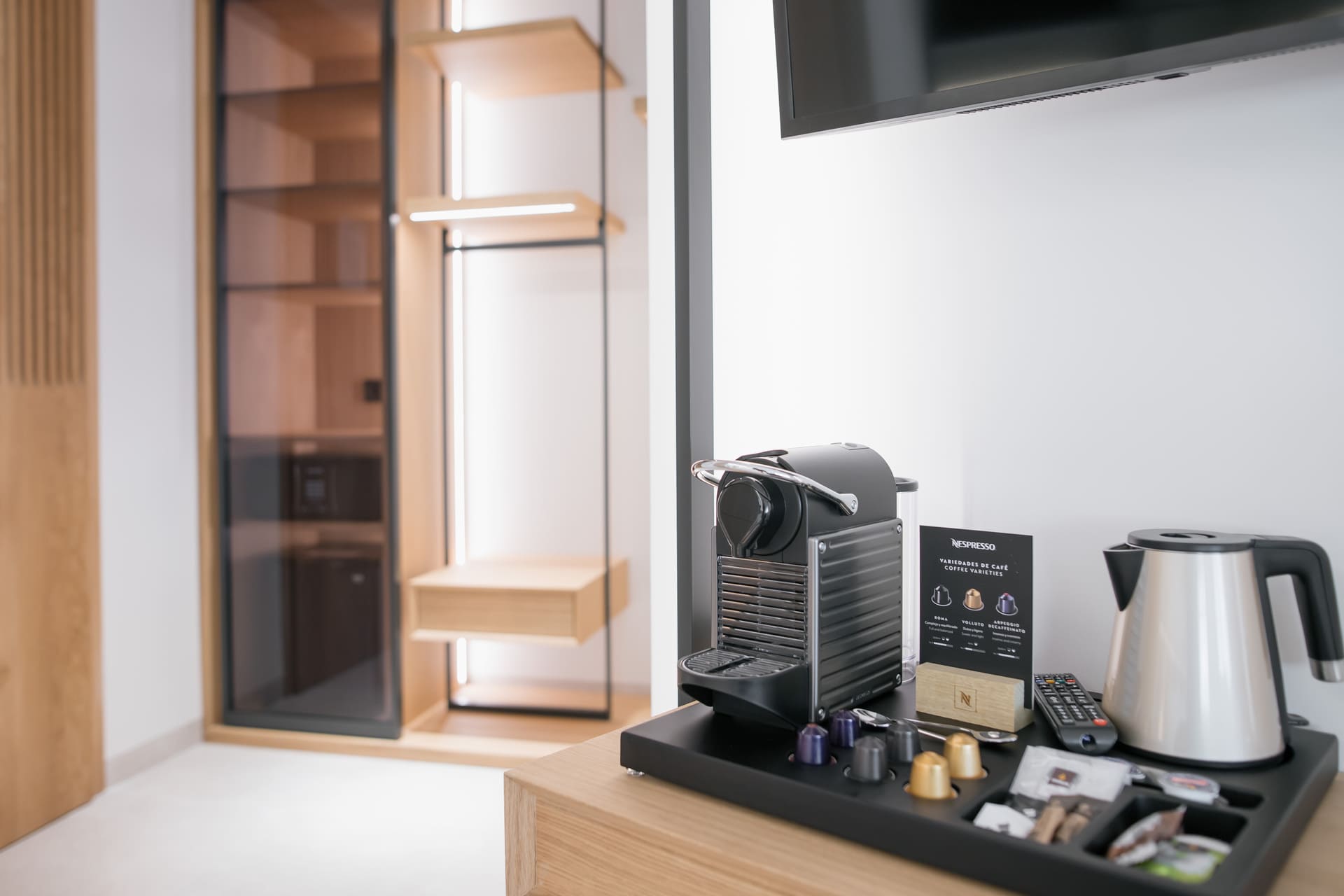 Máquina de café Nespresso y hervidor en habitación; vestidor de madera al fondo.