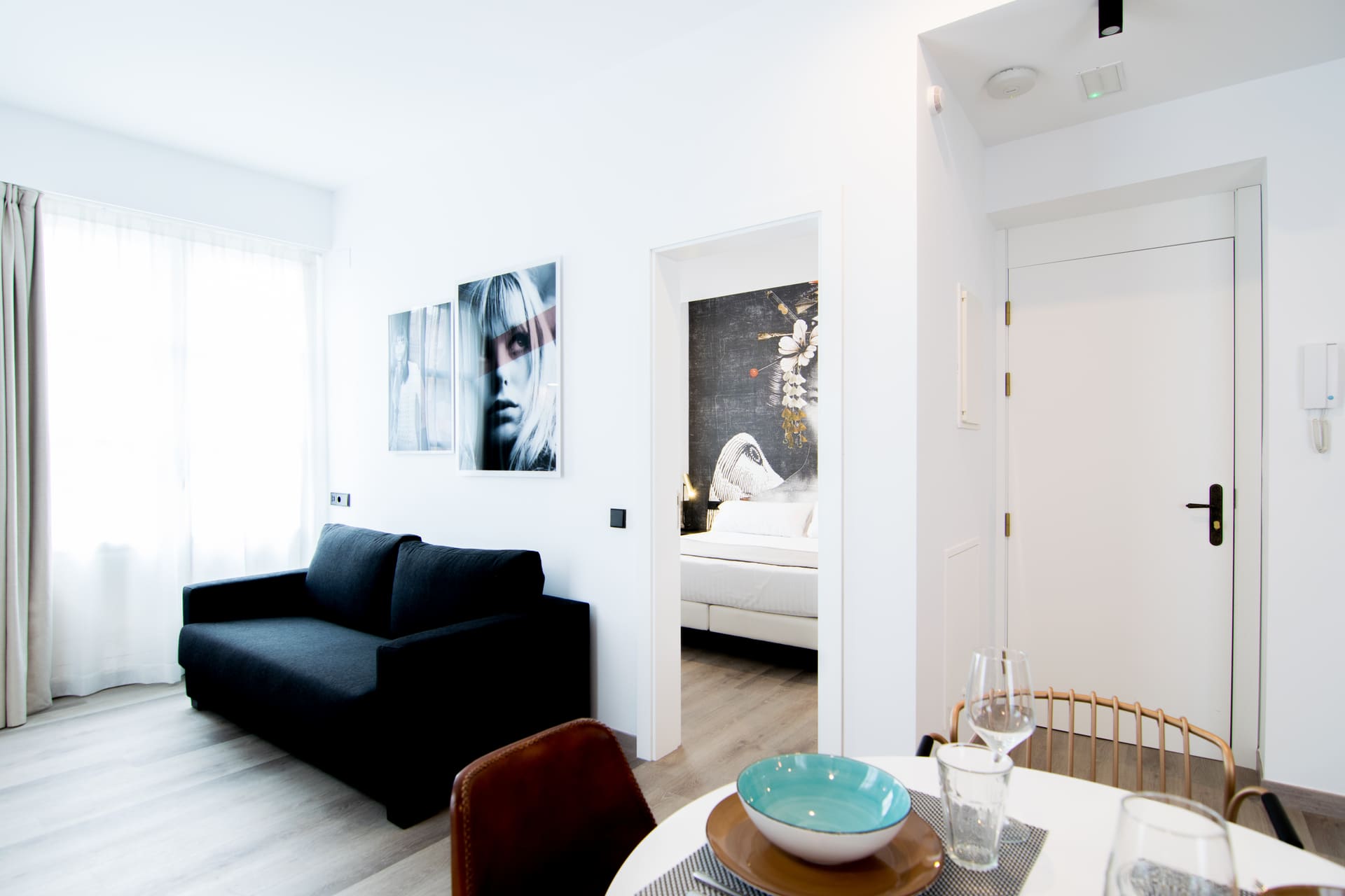 Sala de estar de suite de hotel con sofá negro, comedor y acceso al dormitorio