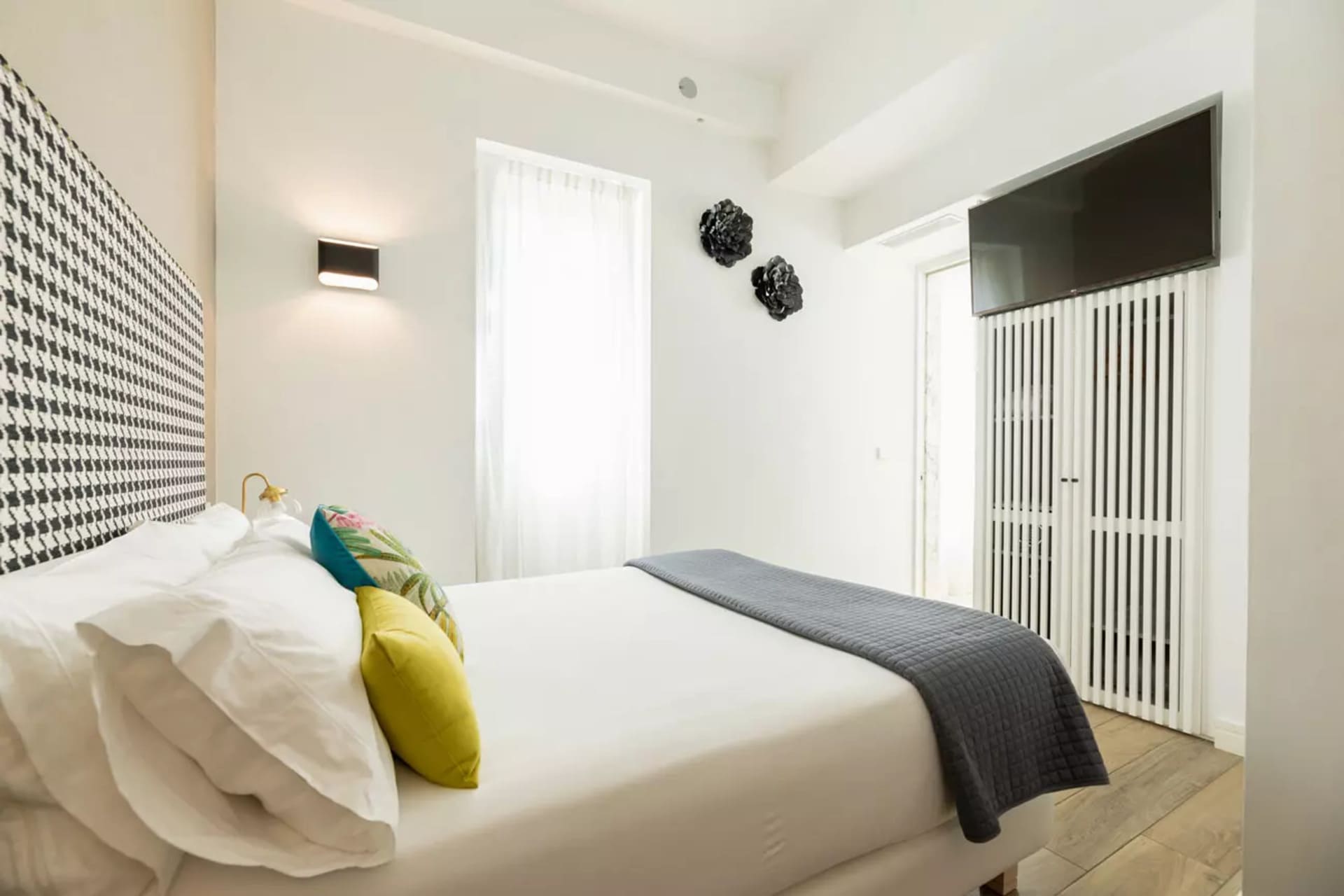 Habitación doble pequeña con cama blanca, cabecera en blanco y negro y cojines coloridos