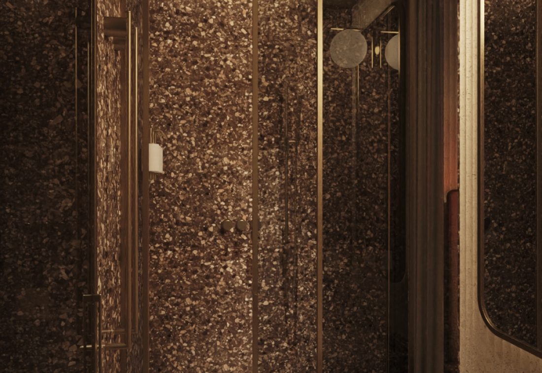 Baño de hotel con ducha de mamparas de vidrio, lavabo de piedra terrazzo y espejo ovalado