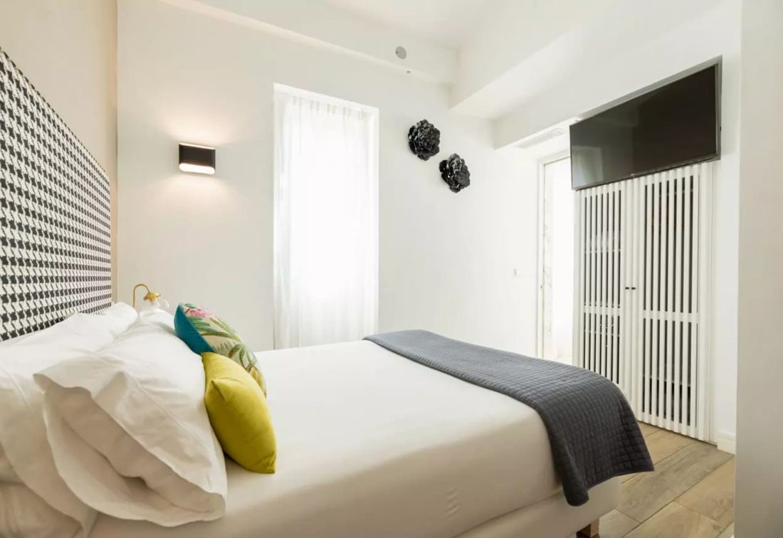 Habitación doble pequeña con cama blanca, cabecera en blanco y negro y cojines coloridos