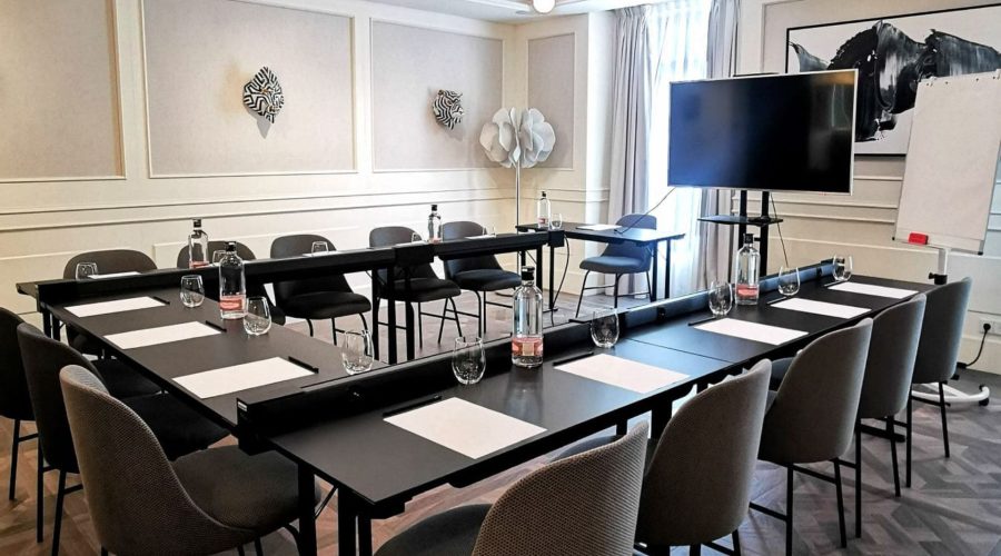 Sala de reuniones corporativas en MYR Hotels con mesas en U, pantalla grande y botellas de agua