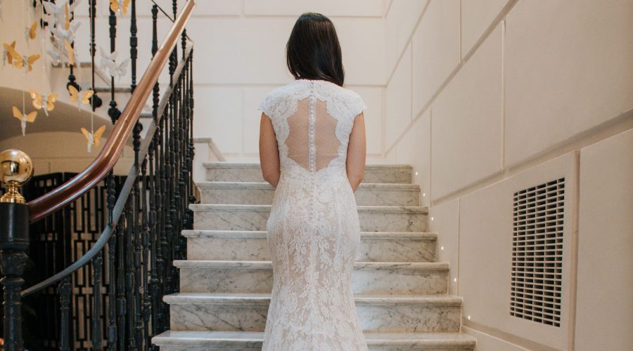 Novia de espaldas con vestido de encaje blanco sube una escalera de mármol en un hotel
