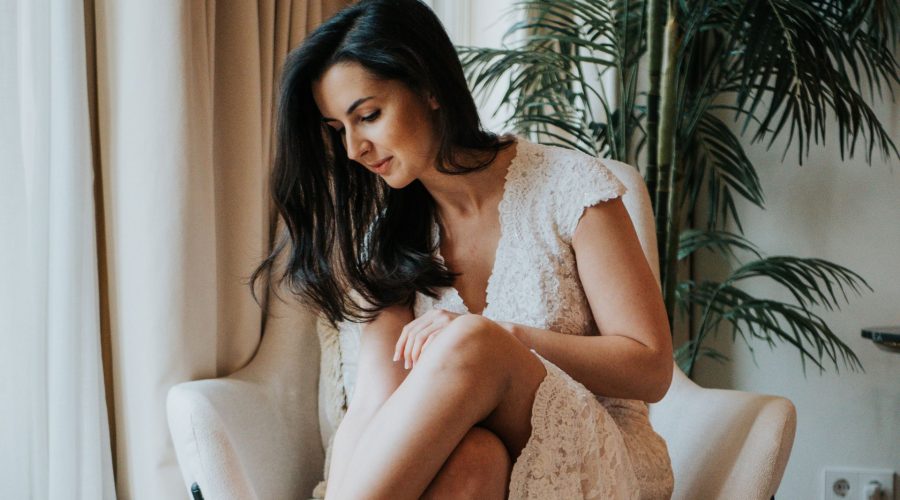 Mujer con bata de encaje blanca, sentada en sillón junto a una planta