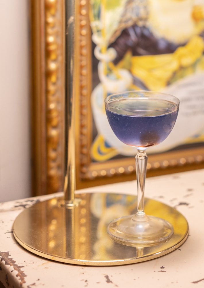 Cóctel azul en copa coupe sobre mesa reflectante, en galería de Madrid