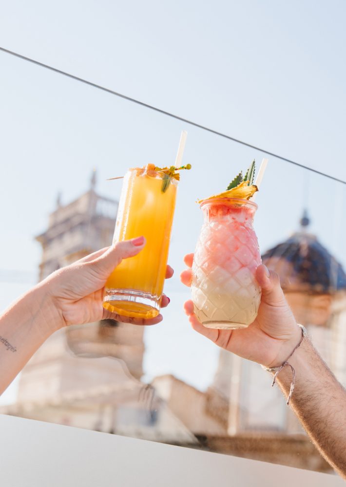 Brindis con dos cócteles en azotea con vistas a la ciudad