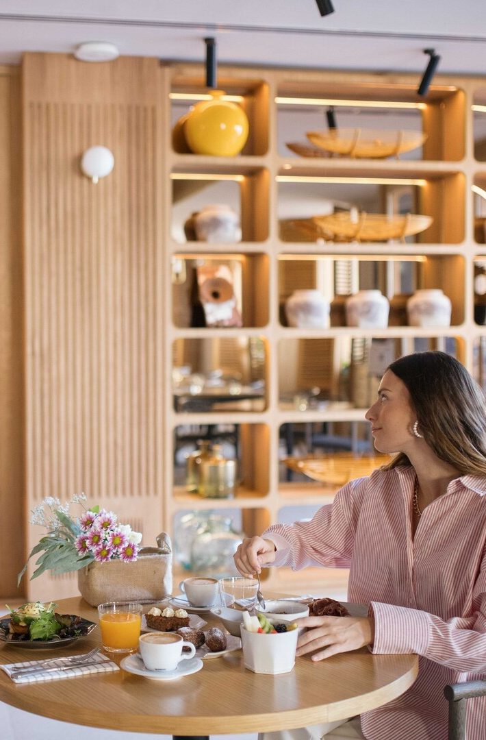 Mujer desayunando en Galería Las Tenerías, mesa con jugo, café y bollería