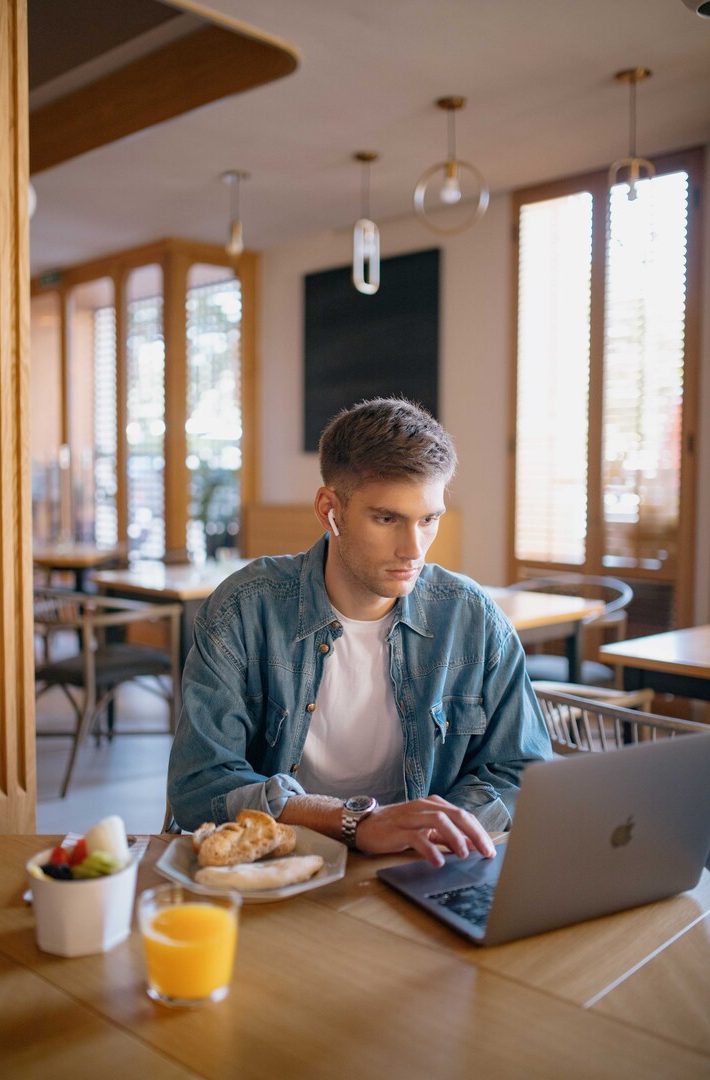 Hombre trabajando en portátil en cafetería de Galería Las Tenerias, con croissant y jugo de naranja