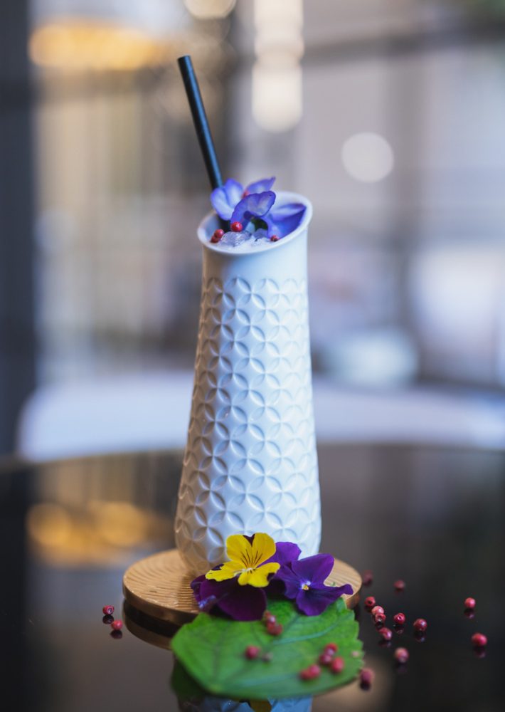 Cóctel en jarrón blanco con flores comestibles moradas y amarillas