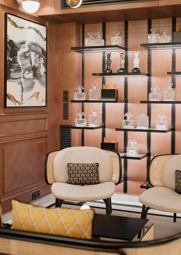 Lounge bar con estanterías de vidrio y decantadores de cristal, dos sillones blancos.