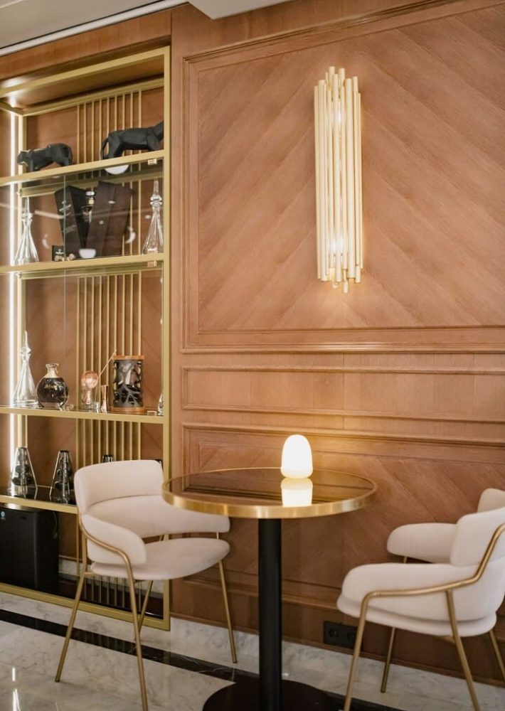 Lladró Lounge Bar: mesa redonda con lámpara y sillas blancas junto a estantería dorada