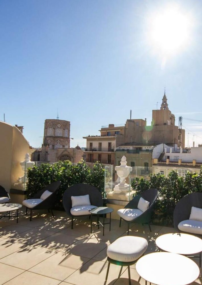 Azotea de lounge bar con sillones curvos y cojines blancos, vistas a la ciudad