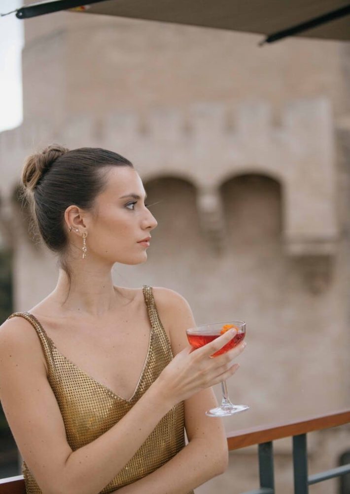 Mujer con vestido dorado en la azotea de Luna Valencia, sosteniendo una copa rosada