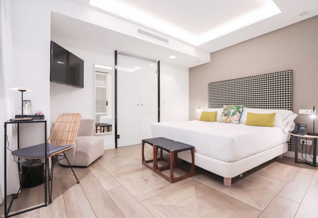 Habitación de hotel con cama king y cabecero estampado, TV y zona de descanso