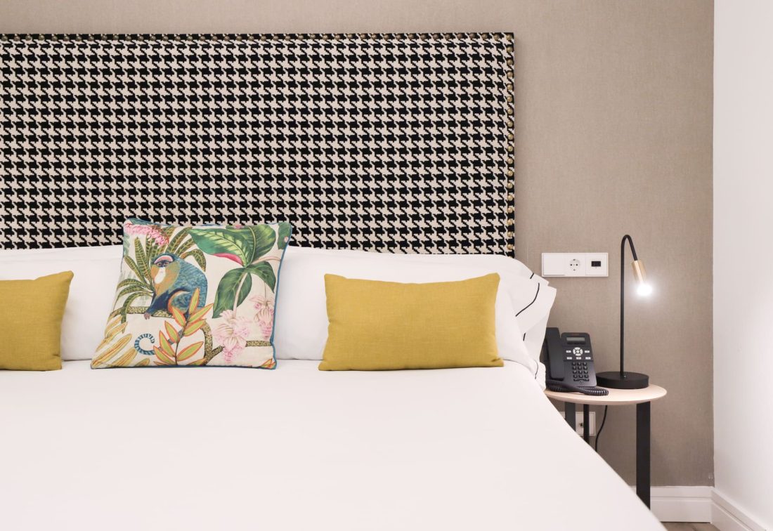 Cama de hotel con cabecera de pata de gallo y cojines amarillos