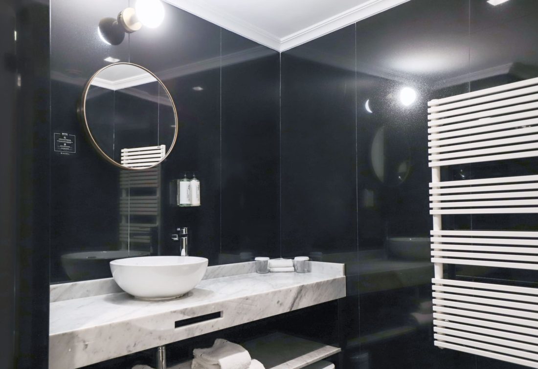 Lavabo blanco de cuenco sobre encimera en baño moderno con espejo circular y toallero radiador blanco