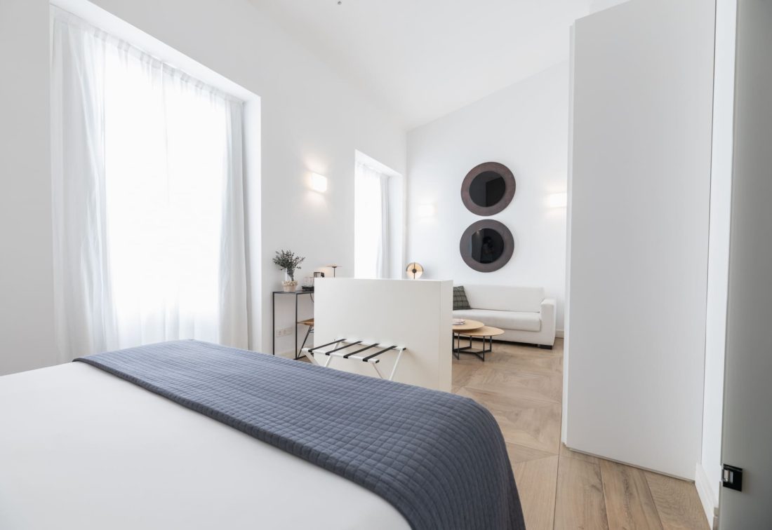 Habitación de hotel moderna con cama en primer plano, sala de estar blanca y espejos circulares