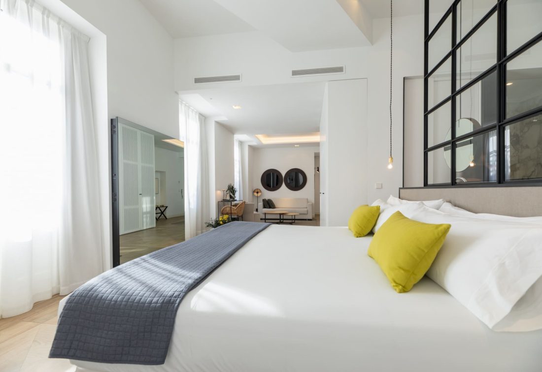 Dormitorio de suite con cama grande, cojines amarillos y separador de vidrio negro