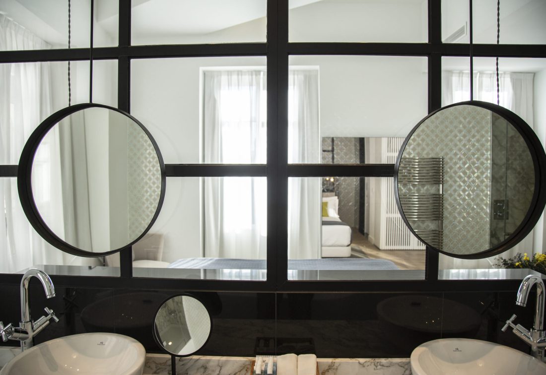 Baño con lavabos dobles y dos espejos circulares frente a la habitación