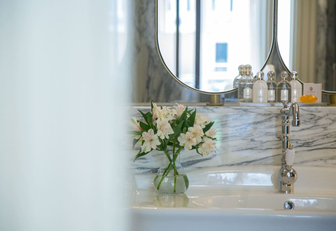 Lavabo de mármol con jarrón de flores blancas en baño de hotel