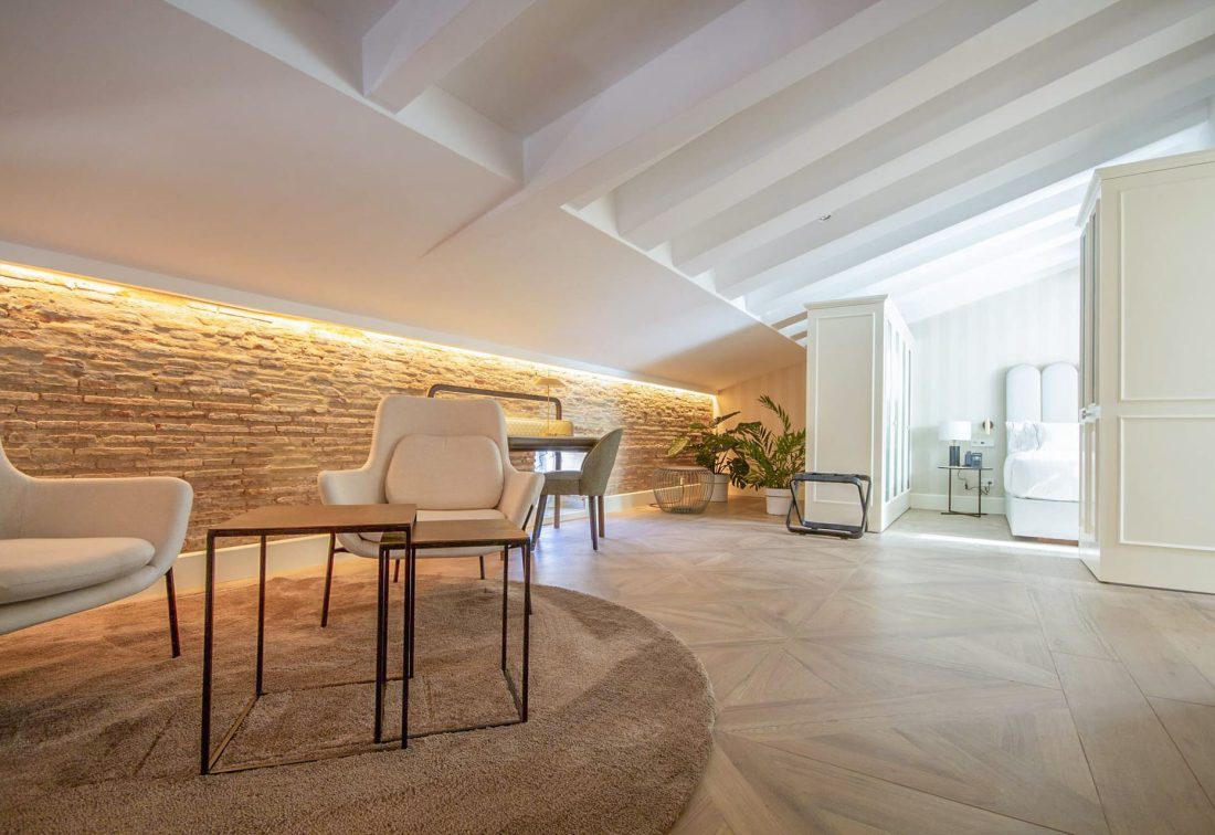 Suite loft con sala de estar y dormitorio en ático; pared de piedra y luz cálida.