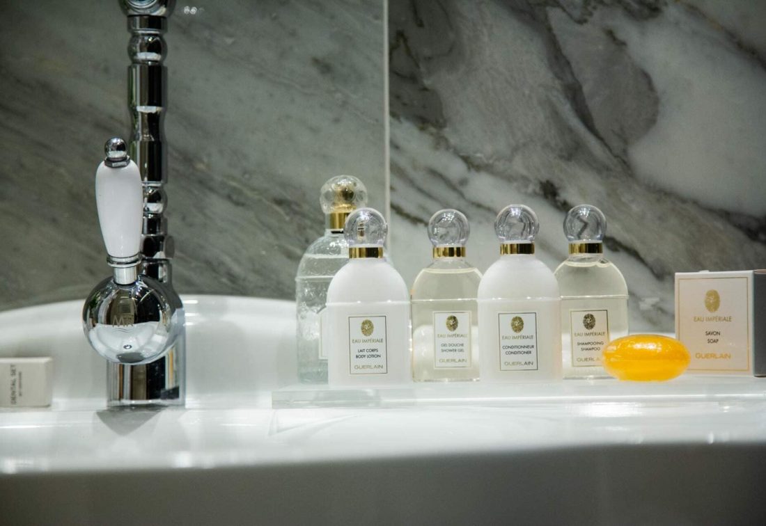 Conjunto de amenities Guerlain en el lavabo del hotel, botellas blancas con tapones dorados y jabón naranja