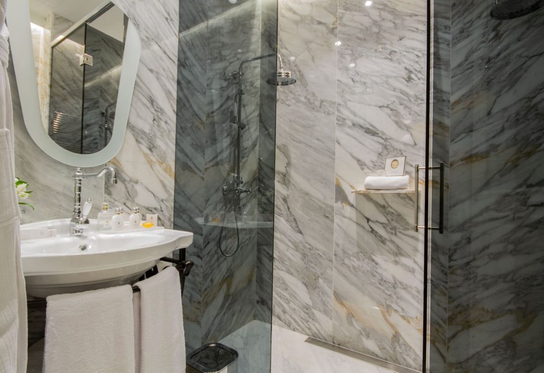 Baño de hotel con lavabo, espejo oval y ducha de vidrio