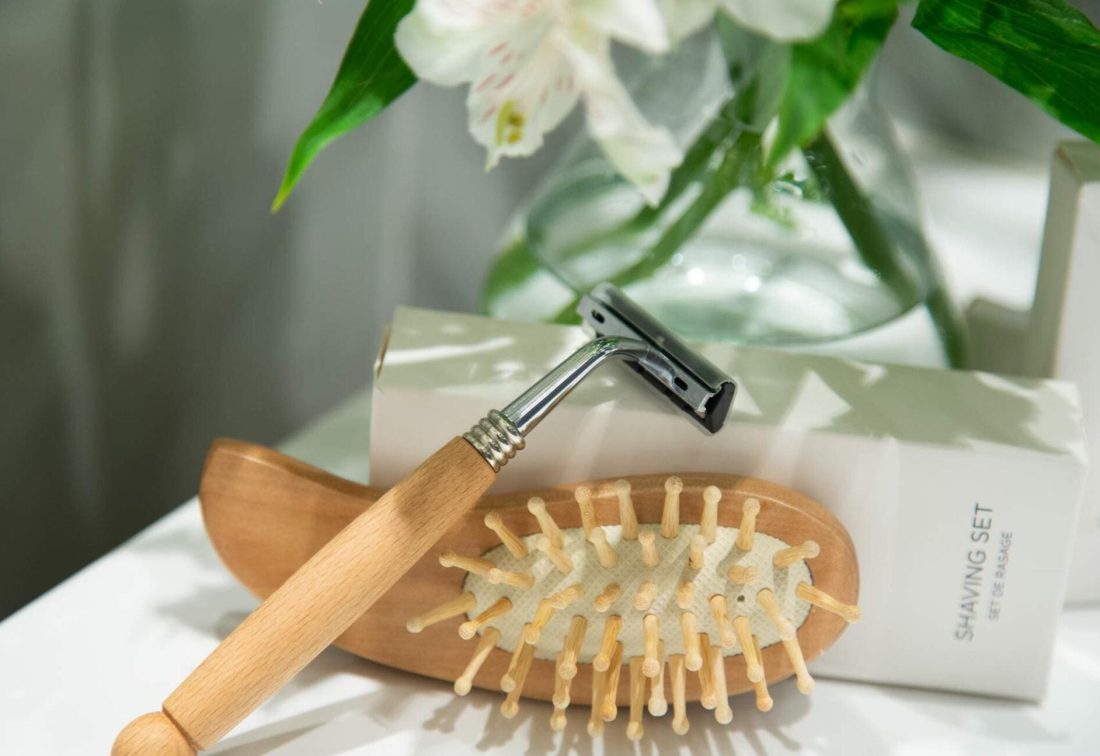 Set de afeitado de madera con brocha y maquinilla, junto a flores en el lavabo.