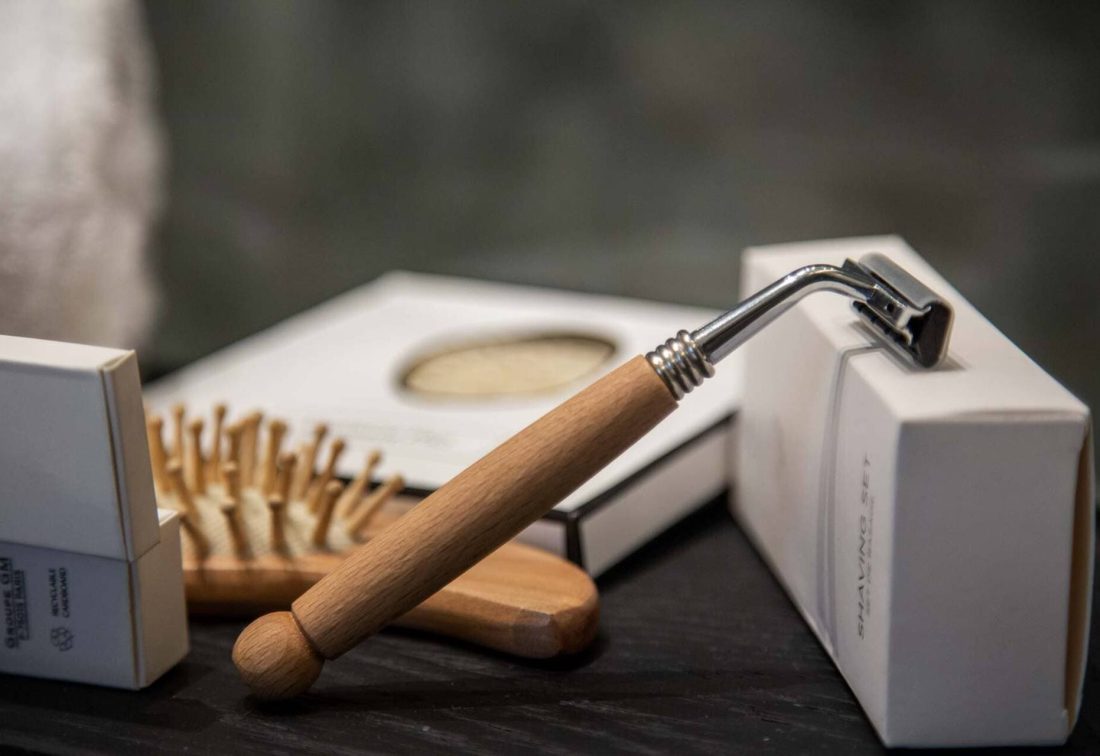 Set de afeitado con maquinilla de mango de madera y cepillo, junto a cajas de productos
