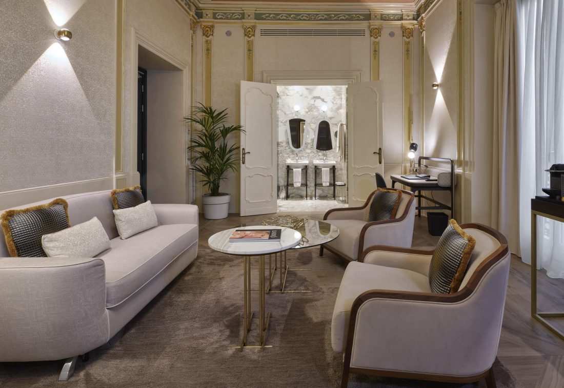 Sala de estar de suite elegante con sofá y sillones frente a baño de mármol