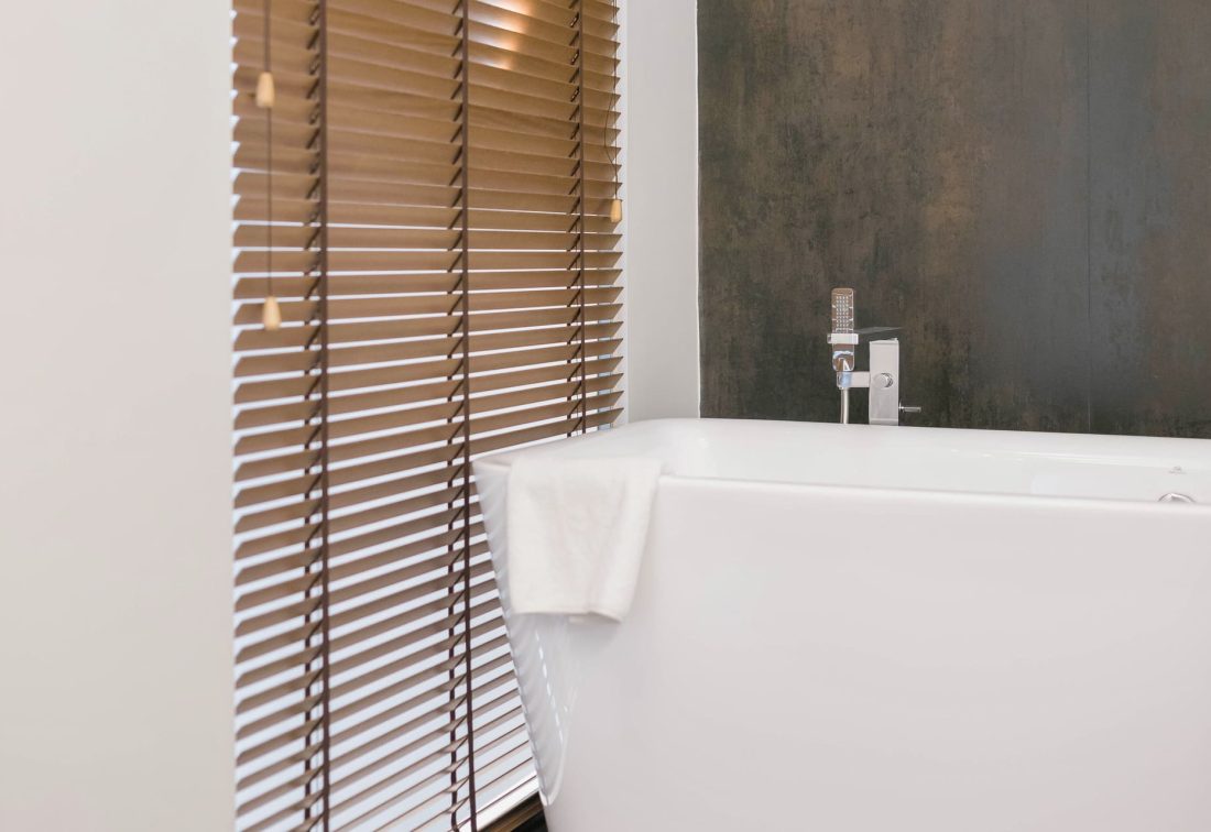 Bañera blanca en baño moderno con persianas de madera y toalla sobre el borde