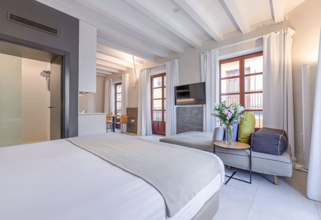 Habitación de hotel amplia con cama y sala de estar junto a ventanales