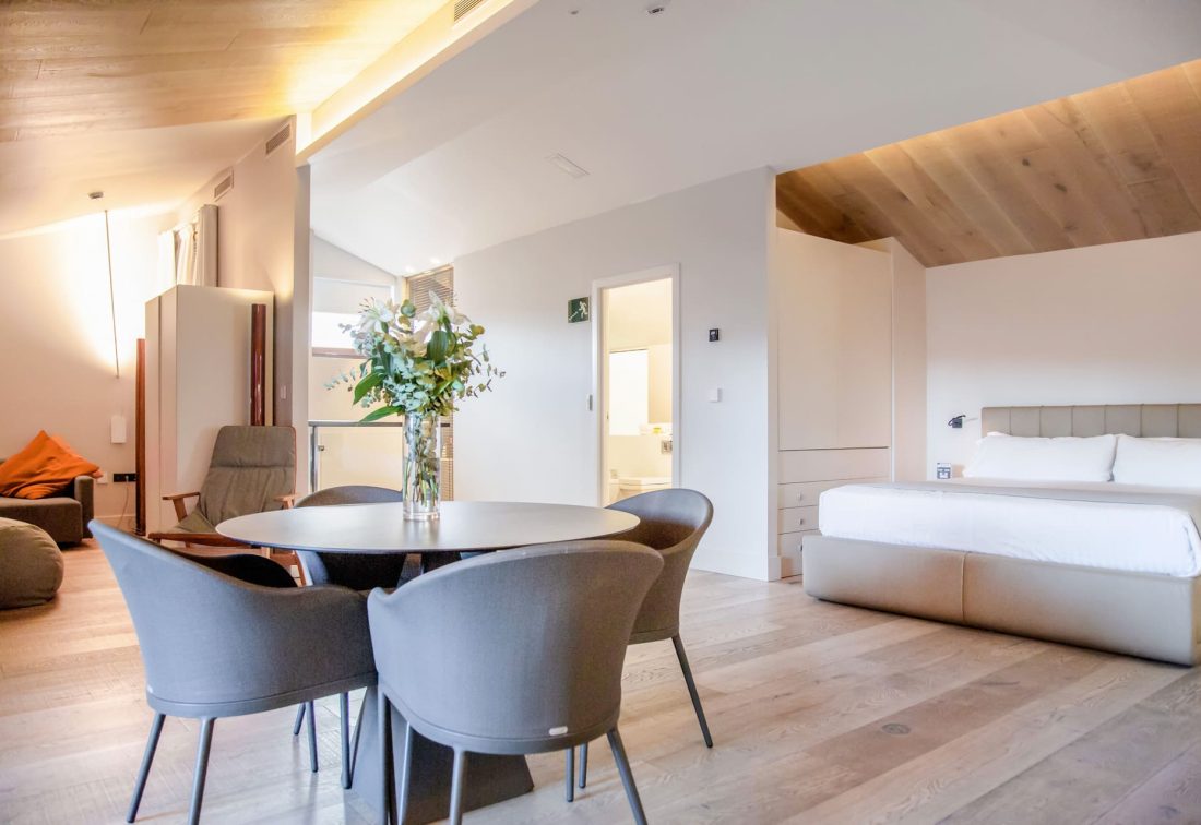 Suite amplia con cama grande y área de comedor con sillas grises