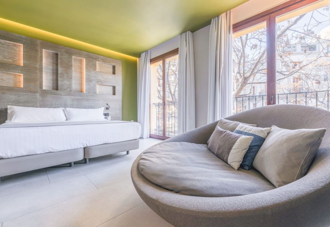 Habitación de hotel moderna con cama king y sofá curvo junto a ventanales