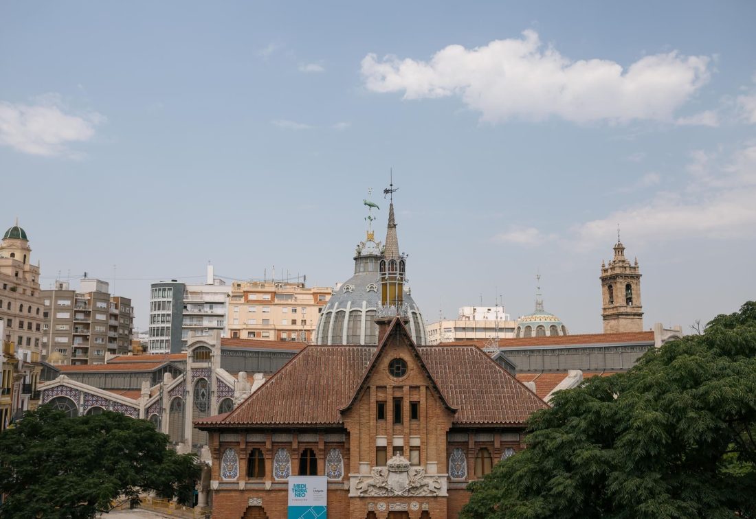 Edificio histórico de ladrillo con techo de tejas rojas y torre con cúpula en skyline urbano