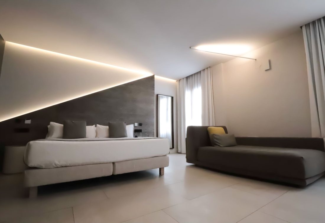 Habitación de hotel moderna con cama grande y sofá gris