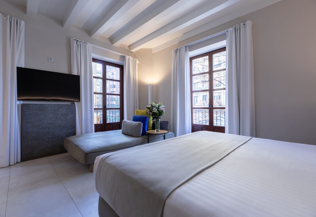 Habitación de hotel con cama king y zona de descanso junto a ventanales