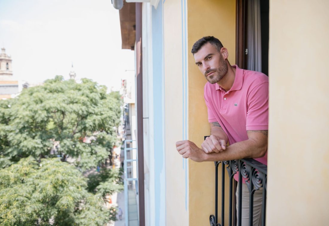 Hombre apoyado en la barandilla de un balcón de edificio urbano