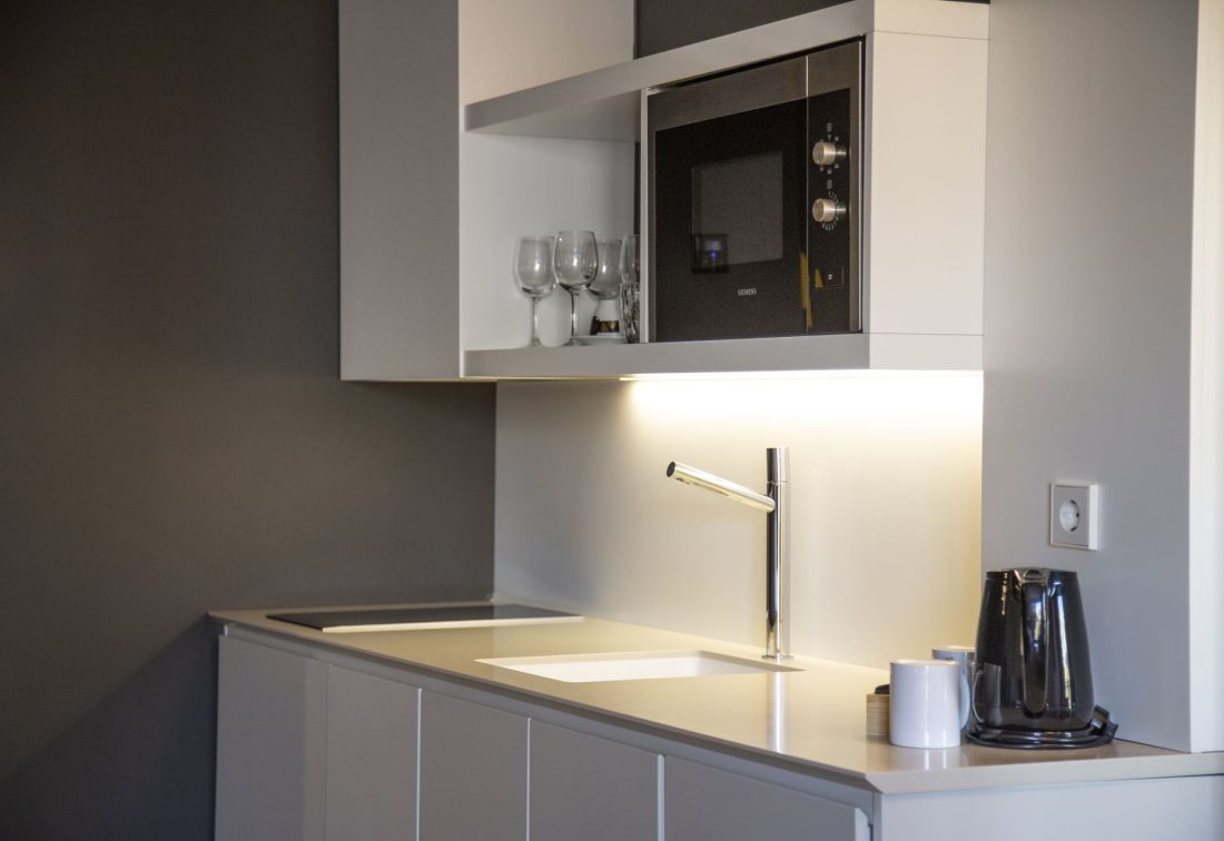 Cocina moderna de hotel con fregadero y grifo cromado, microondas empotrado y cafetera.