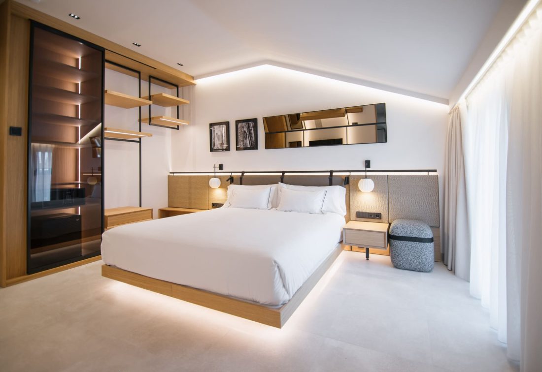 Habitación de hotel moderna con cama king-size, mesitas y espejo decorativo.