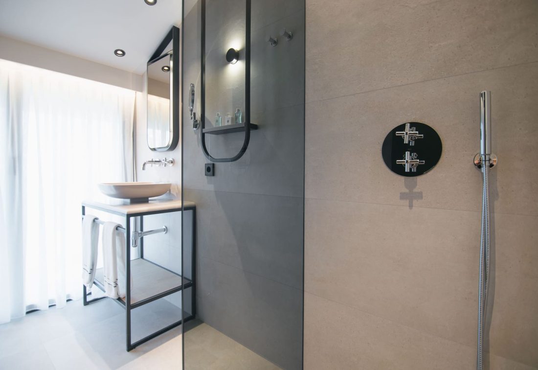 Baño moderno de hotel con lavabo de cuenco sobre mueble metálico y ducha.